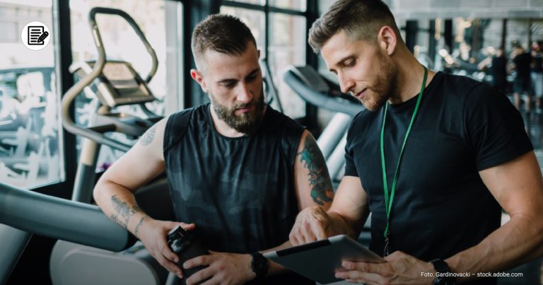 zwei Männer im Fitnessstudio schauen sich einen Trainingsplan an